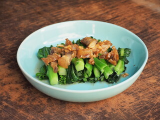 crispy fried pork belly on top of fried bok choy vegetable in a dish on wooden background