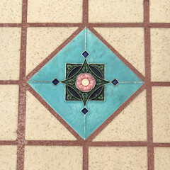 Old floral tile of aqua with pink flower set into sandstone tile pattern with terra-cotta red grout.