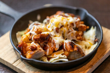 スキレットに盛り付けられた、熱々のチーズタンドリーチキン。香ばしく焼き上がったスパイシーなチキンに、とろりと溶けた濃厚なチーズが絡む一皿です。箸で持ち上げた際のチーズの伸びや、立ち上る湯気が食欲をそそる調理イメージ。 | Tandoori chicken with melted cheese being lifted by chopsticks in a skillet.