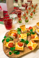 Obraz na płótnie Canvas square slices of quiche with cherry tomatoes and corn lettuce leaves on a wooden cutting board, appetizer table with snacks and canapes