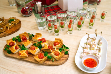 square slices of quiche with cherry tomatoes and corn lettuce leaves on a wooden cutting board, appetizer table with snacks and canapes