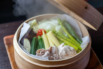 和食レストランで提供される、ヤングコーンやアスパラガスなど色鮮やかな夏野菜と豚肉のヘルシーなせいろ蒸し。湯気が立ち昇るシズル感のあるアップ写真