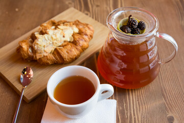 Breakfast in the cafe. juniper tea with lime served in a glass pot, a cup of hot tea and a croissant with almonds.