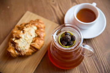 Breakfast in the cafe. juniper tea with lime served in a glass decanter, a cup of hot tea and a croissant with almonds.