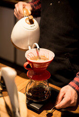 the barista spills hot water and makes coffee using the funnel method. the barista works behind the counter.