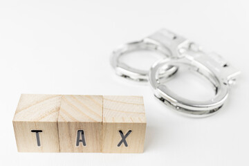 木のブロックのTAXと、玩具の手錠。脱税のイメージ