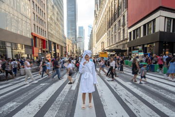 Woman in bathrobe with cup of coffee is staying on crosswalk with passing people on background....