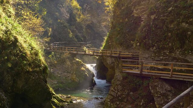 Stunning scenic overview of Vintgar gorge with river and wooden path in autumn. Beautiful sightseeing location between steep rocky slopes. Gorgeous color palette of autumn foliage above green river.