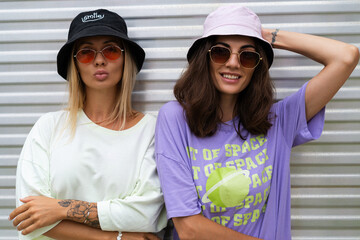 Two young positive stylish hipster smiling girl friends in trendy panama and trendy sunglasses posing outdoor, having fun, laugh