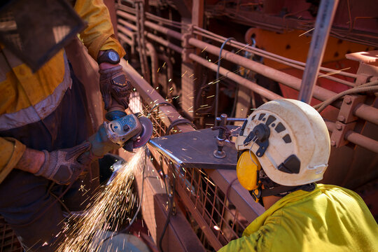 Supervisor construction worker wearing side impact rope access safety white helmet attached with yellow noise disruptive earmuffs protection while worker is performing grinding preparation steel plat 