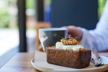 Closeup image of a woman holding and drinking coffee with a piece of carrot cake on the table