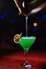 Bartender's hand pours a green cocktail close-up. A glass with a long stem. The bartender prepares drinks for guests. Night life, club life. Great serving of cocktails. Amazing cocktails
