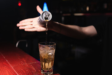Bartender's hand pours an energy drink into a glass. The bartender prepares drinks for guests....