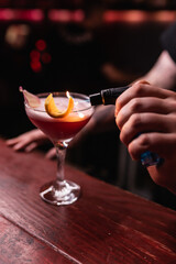 The bartender lights a lemon on an alcoholic cocktail with a lighter. The bartender prepares drinks for guests. Night life, club life. Great serving of cocktails. Amazing cocktails