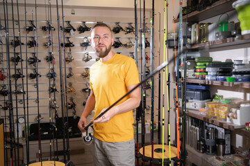 Young fisherman man chooses a fishing rod in a fishing store