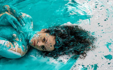impressive portrait of adult brunette curly woman, crossing her arms over her chest, a lot of green turquoise and orange color paint, decorative creative expressive abstract body painting