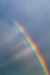 The sun's rays shine on a multi-colored rainbow from behind the clouds. Vertical photo