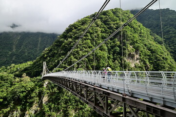 Fototapeta na wymiar Buluowan Terrace in Taroko National Park - Steep canyon spanned by a footbridge. A modern suspension footbridge spans this steep, densely forested gorge in a popular hiking area.