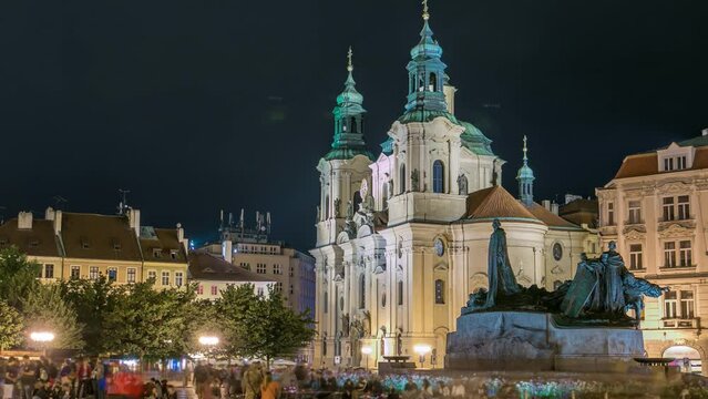 Baroque St. Nicholas' Cathedral on the Oldtown Square in Prague with monument Jan Hus illuminated at night timelapse. Tourists walk around