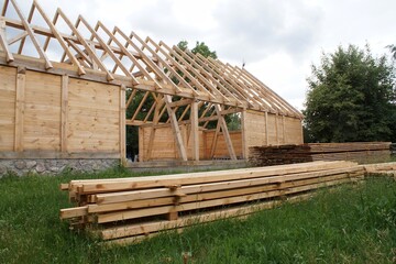 A wooden farm building under construction and the planks and beams lying in front of it.