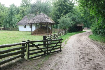 A dirt road that runs along the fence and the old thatched wooden farmhouse.