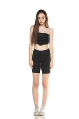 Fototapeta premium Young woman in black shorts and top posing in the studio on white.