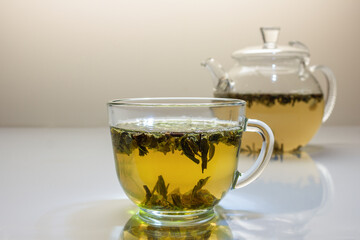 glass cup and teapot with green leaf tea on white glass table