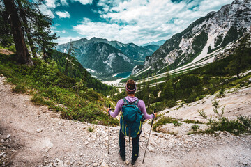 Fototapeta premium Young woman enjoys beautiful view from hiking trail on Baires Lake in the Dolomite mountains in the afternoon. Braies Lake (Pragser Wildsee, Lago di Braies), Dolomites, South Tirol, Italy, Europe.