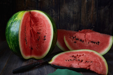 A sliced watermelon lies on a dark wooden table, next to a dish with sliced ​​watermelon slices. Dark key.