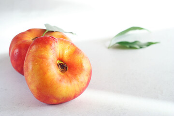 Two peaches lie on a light table, leaves lie nearby. Sunny morning