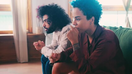 Young Arabian man and African American woman cheer for their favorite football team and start screaming with joy after winning watch game on TV sits side by side on couch in your own appartment
