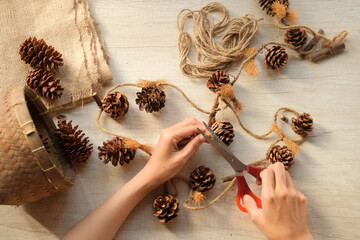 Woman's hands make wall decoration from pine cones and jute rope