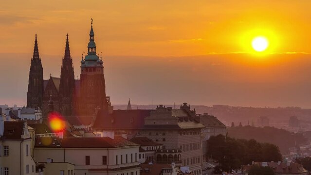 A beautiful view of Prague at sunrise on a misty morning timelapse. Prague Castle and St. Vitus Cathedral on the left and a golden rising sun above clouds. Close up view