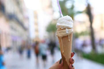 melting ice cream cone in human hand closeup photo on city center background