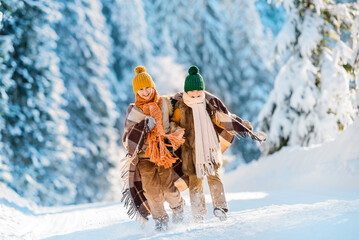 Happy family wrapped in a woolen plaid walking along the snowy road among the beautiful winter nature. Wonderful winter sunny day.