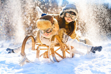 Two smiling children ride lying on a wooden retro sled on a sunny winter day. Active winter...