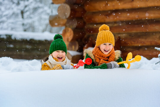 Two small smiling children have fun making snowballs with toy plastic maker. Kids playing snowballs among the snowdrifts. Winter games outdoors. Place for text.