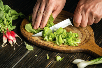Cook hands cutting green lettuce leaves on a cutting board with a knife for preparing a vegetarian dish. Peasant foods