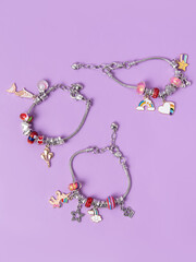 Three small silver charm bracelets with many charms on purple background. Creating jewelry. Children's bracelets