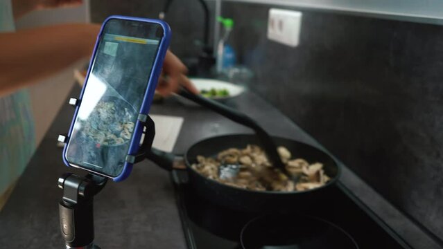 Chef blogger cooking meal and recording video for blog. Young woman cook and filming himself on smartphone for culinary blog while preparing healthy meal with vegetables in kitchen. 4k footage