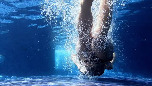 A young sexy woman jumps into the pool and splashes in the crystal clear water. Unrecognizable girl swimming underwater in the hotel pool on a sunny day. Lady is resting during summer holidays. 