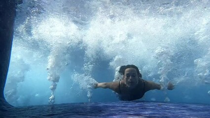 A young sexy woman swims in the pool and splashes in the crystal clear water. Unrecognizable girl swimming underwater in the hotel pool on a sunny day. Lady is resting during summer holidays. 