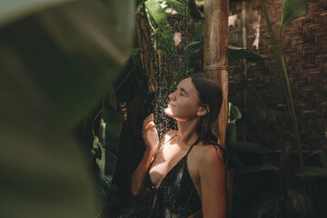 Slim woman in a black swimsuit in the shower in a tropical garden. Organic skin care. Lifestyle, holidays in Bali