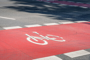 rote Fahrbahn mit weißem  Fahrrad Symbolquer von links nach rechts mit Schatten eines Baumes auf...
