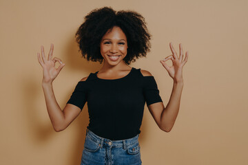 Young african female shows ok sign okay gesture with both hands, isolated over beige background