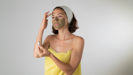 Fototapeta premium Woman in a towel makes a face mask - home care for the skin of the face