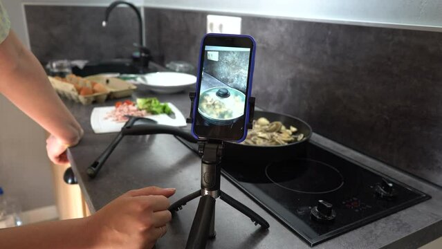 Chef girl blogger cooking meal and recording video for blog. Young woman cook and filming himself on smartphone for culinary blog while preparing healthy meal with vegetables in kitchen. 4k footage