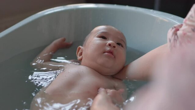 Cute baby having bath. Mother holds and bathes baby