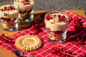 Dessert im Glas mit Johannisbeeren, Vanillecreme und Keks auf einer roten Tischdecke im Sonnenlicht