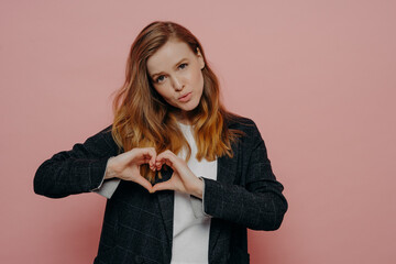 Attractive young woman in formal wear showing heart shape sign